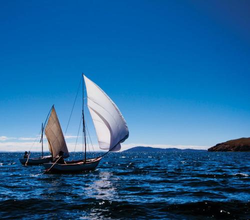 a boat with a white sail in the water at titicaca lodge - LUQUINA in Luquina