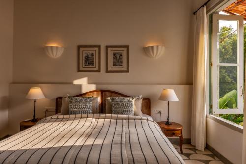 a bedroom with a bed with two lamps and a window at La Rozalia, Exquisite 4 BHK Villas with Large Pool, Garden, Dedicated Caretaker, Terrace, 2 mins from the famous Dear Zindagi Road in Mapusa