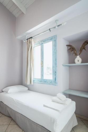 a white bedroom with a bed and a window at PARALIA Stoudios in Parga