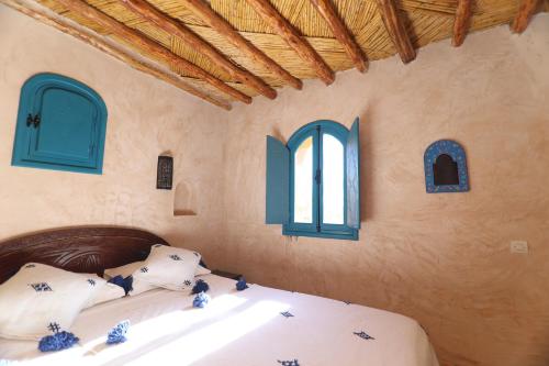 a bedroom with a bed with white sheets and blue windows at Paradis Nomade in Azrarag