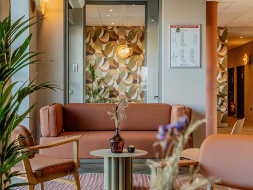 a lobby with a couch and tables and plants at B&B HOTEL Maubeuge Gare in Maubeuge