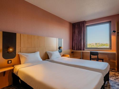 a hotel room with two beds and a window at B&B HOTEL Maubeuge Gare in Maubeuge