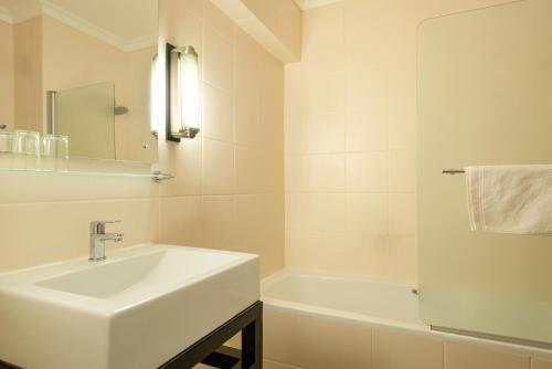 a white bathroom with a sink and a bath tub at Mercure Hotel Windhoek in Windhoek