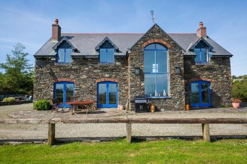 a stone house with blue windows and a wooden fence at Schull Coastal rural hideaway 5 night min in Derreennatra