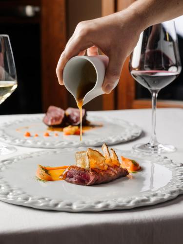 a person pouring sauce onto a plate of food at Montana Lodge & Spa, by R Collection Hotels in La Thuile