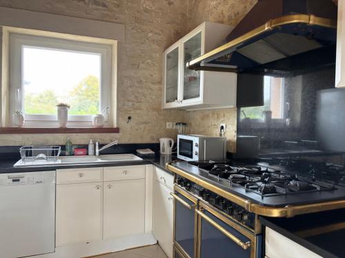 a kitchen with white cabinets and a stove top oven at Le So Art, grande maison 4 chambres, terrain de pétanque, grand jardin clos, flipper, babyfoot, jeux Arcade, ping pong,1 km mer, proche golf, Port en Bessin, Bayeux et plages du débarquement, adaptée enfants in Commes