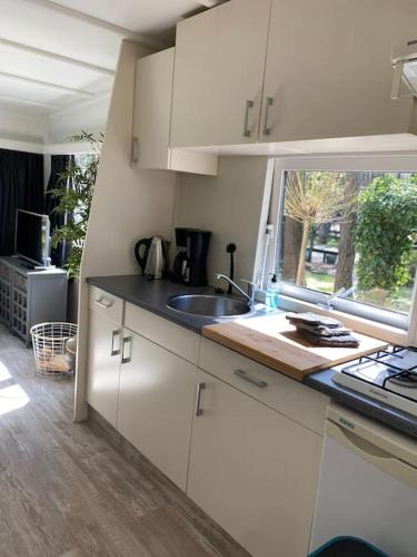 a kitchen with white cabinets and a sink and a window at Prachtig Boschalet met CV, Airco en Sauna op de Veluwe in Doornspijk