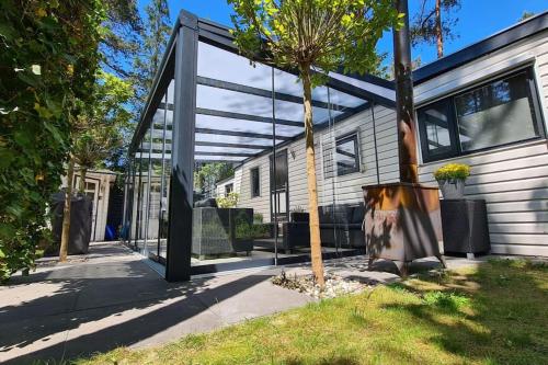 a glass extension to a house with a tree at Prachtig Boschalet met CV, Airco en Sauna op de Veluwe in Doornspijk