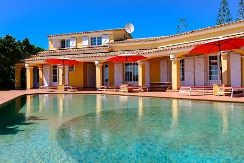 - une piscine en face d'une maison avec des parasols rouges dans l'établissement VILLA ISOLELLA-4 chambres, pieds dans l'eau Presqu'ile de L'ISOLELLA, à Pietrosella