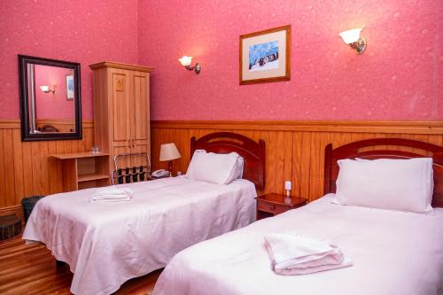 a bedroom with two beds and a pink wall at Hotel Plaza in Punta Arenas