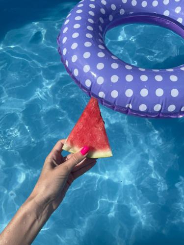 a hand holding a slice of watermelon next to a swimming pool at Golden Sand in Plaka