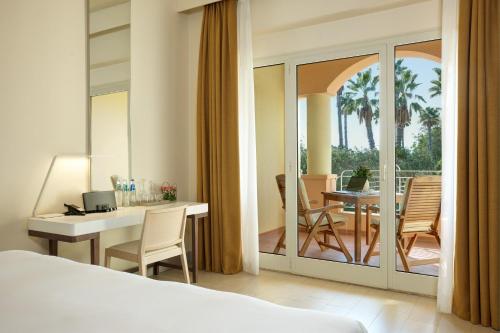 a bedroom with a bed and a desk and a balcony at Almar Timi Ama Resort & Spa in Villasimius