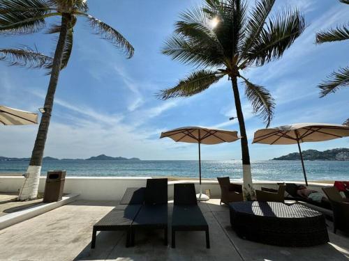 a patio with chairs and umbrellas on the beach at Vista al Mar, Terraza y Albercas in Manzanillo
