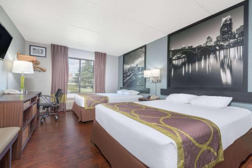 a hotel room with two beds and a desk at Super 8 by Wyndham Bloomington/Airport in Bloomington