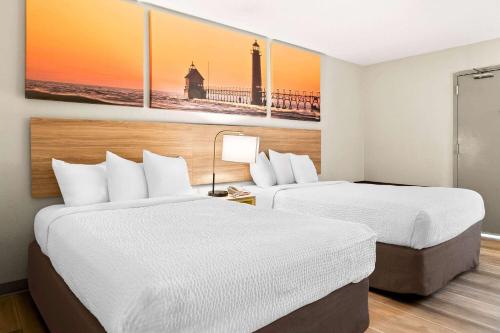two beds in a hotel room with two paintings on the wall at Days Inn & Suites by Wyndham Warren in Warren