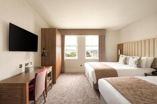a hotel room with two beds and a desk at voco The Clifton Folkestone by IHG in Folkestone