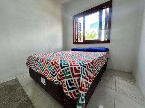 a bedroom with a bed with a colorful comforter and a window at Tranquilidade e água fresca! in Tramandaí