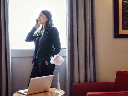 a woman standing by a window talking on a cell phone at Pullman Paris La Défense in Courbevoie
