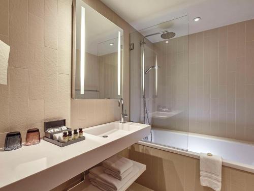 a bathroom with a sink and a mirror and a tub at Pullman Paris La Défense in Courbevoie