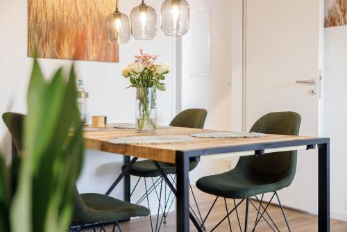 a dining room table with green chairs and a vase of flowers at VISTAMO Dorsten-Rhade, modernes Apartment in Dorsten