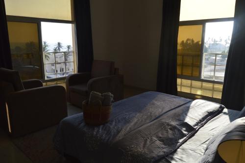 a bedroom with a bed and two chairs and windows at Beautiful Salalah Beach Apartments - 1 by Beautiful Salalah Tours in Salalah