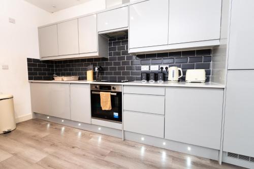 a kitchen with white cabinets and black tiles at Cosy 1Bed Getaway in Central Hull in Hull