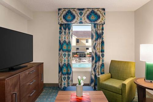 a living room with a television and a chair and a window at Homewood Suites by Hilton Fort Myers in Fort Myers