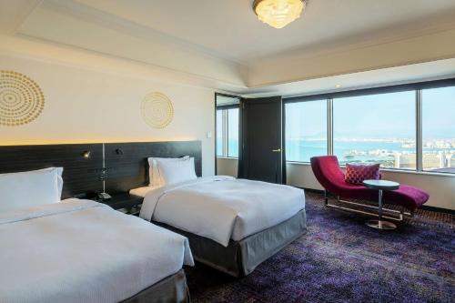 a hotel room with two beds and a red chair at Hilton Fukuoka Sea Hawk in Fukuoka