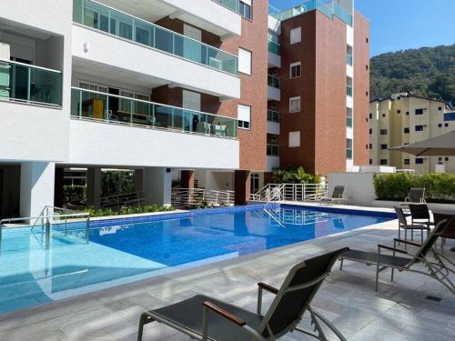 Una gran piscina con sillas y un edificio. en Cobertura Santorini Nova com Spa e Solário na Praia Grande, en Ubatuba
