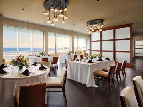 a dining room with white tables and chairs and the ocean at Embassy Suites by Hilton Myrtle Beach Oceanfront Resort in Myrtle Beach