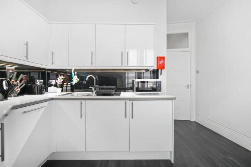 a white kitchen with white cabinets and a sink at Charming Studio Next to Leicester Sq in London