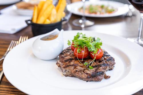 a piece of steak with tomatoes on a white plate at voco The Clifton Folkestone by IHG in Folkestone