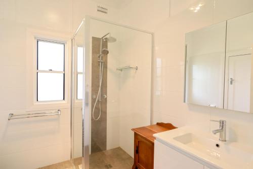 a white bathroom with a shower and a sink at Cosy Sun-Filled Cottage in Tenterfield
