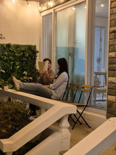 two women sitting on a bench with a laptop at Soban Stay in Busan