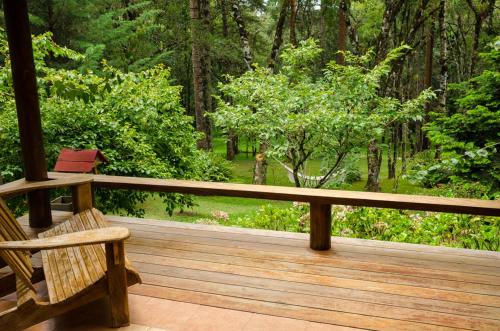 a wooden porch with a bench and trees at Chalés Recanto da Fonte Monte Verde - MG in Monte Verde