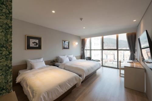 two beds in a hotel room with a large window at Hound Hotel Changwon Jinhae in Changwon