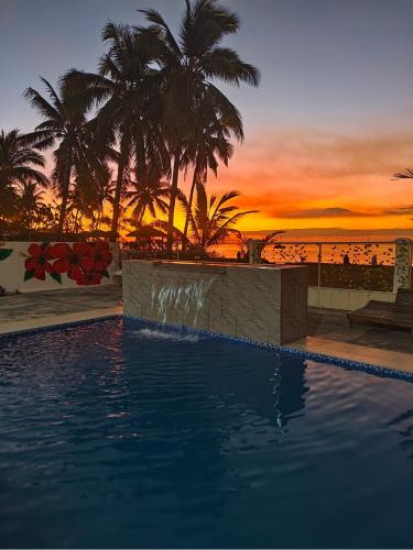 a swimming pool with palm trees and a sunset at Marlin House in Nadi