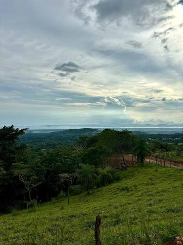 a green field with trees and a cloudy sky at Cabaña con piscina y vista al mar in Puntarenas