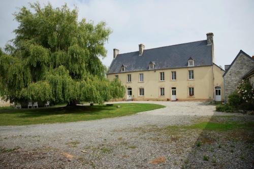 une grande maison avec un arbre devant dans l'établissement Chambre Des Prés à la ferme de Franqueville, à Sainte-Marie-du-Mont