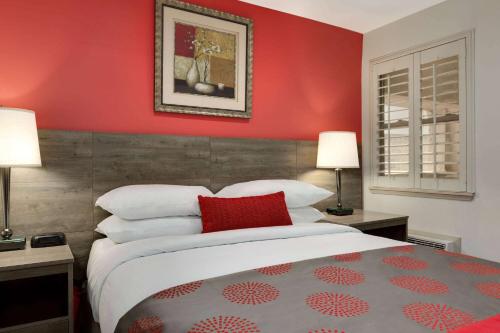 a bedroom with a red wall with a bed and two lamps at Ramada by Wyndham Oakland Downtown City Center in Oakland