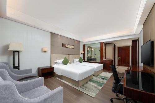 a bedroom with a bed and a tv and chairs at Wyndham Garden Foshan Nanhai in Foshan