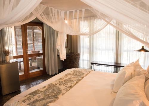 a bedroom with a bed with white curtains and a table at La Lechere Guest House in Phalaborwa