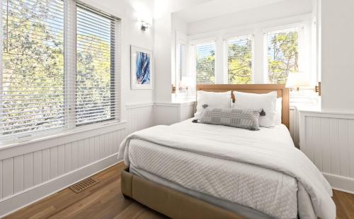 a white bedroom with a large bed with windows at Just For Fun Carriage House in Santa Rosa Beach