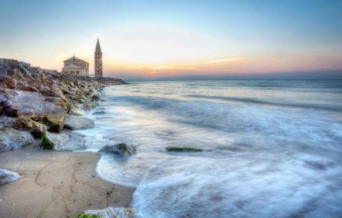 a lighthouse on the shore of a beach at sunset at Ferrari Apartments Ponente in Caorle