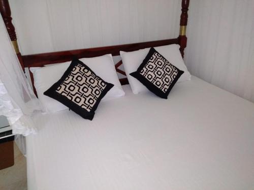 a white bed with three pillows on it at New Well House Apartment in Weligama