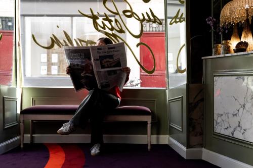 a person sitting on a bench reading a newspaper at Hôtel du Petit Moulin, Haute Couture hotel by Lacroix in Paris