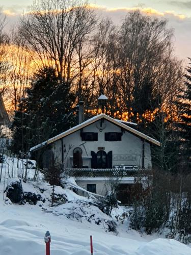 a white house in the snow with a sunset in the background at Unser Woidhaisl - idyllisches Ferienhaus im Bayerischen Wald in Neukirchen