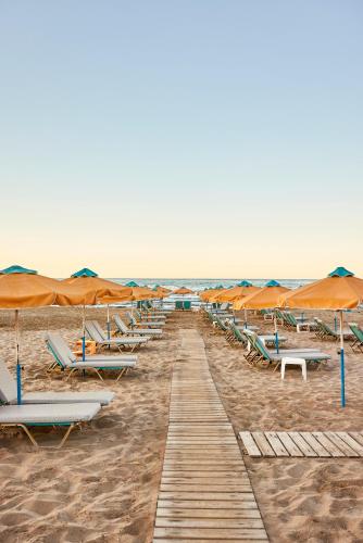 a row of lounge chairs and umbrellas on a beach at Vlachakis Hotel in Stalida