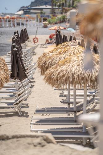 a row of straw umbrellas and chairs on a beach at Residence Borgomare in Albenga