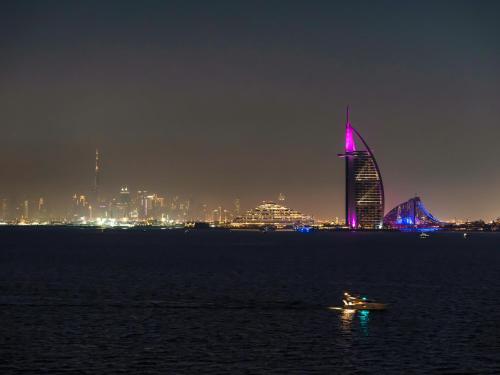 a boat in the water with a city at night at Luxury Apartments in Anantara Resort with Stunning Burj AlArab & Sea Views in Dubai